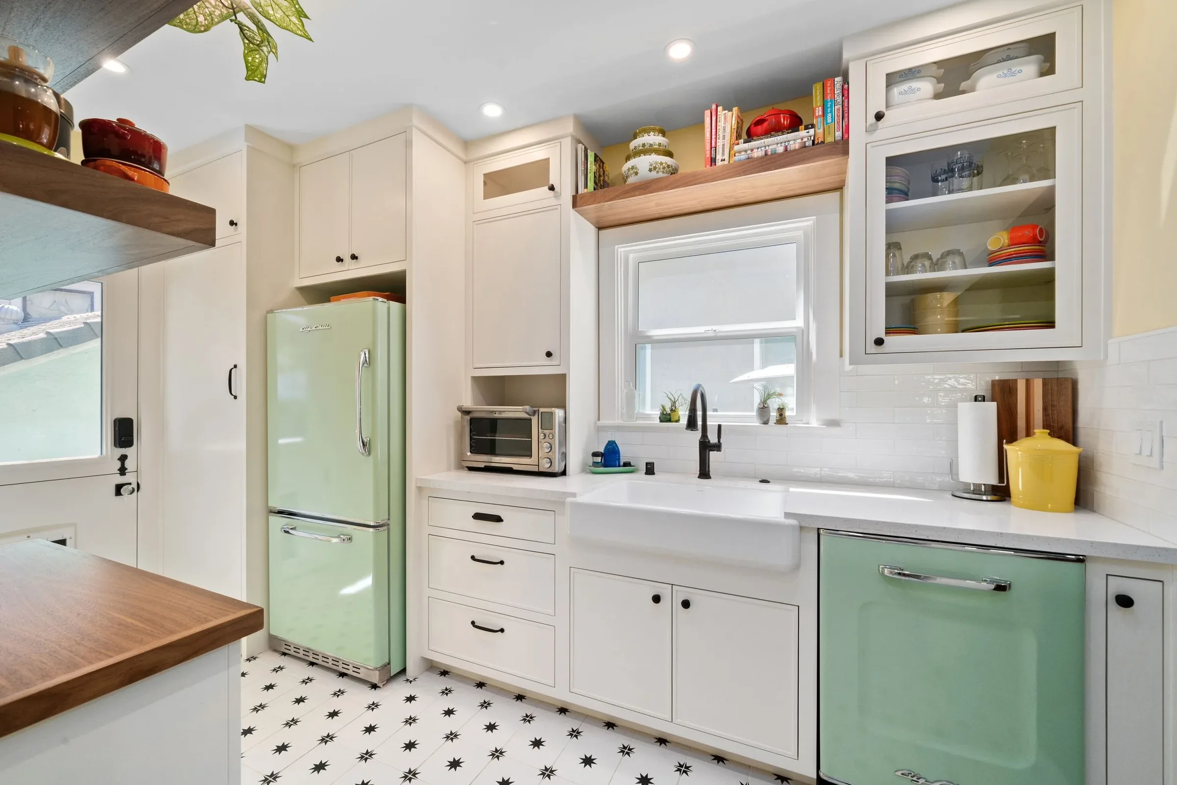 Kitchen with white cabinetry, a white farmhouse sink, a green vintage refrigerator, open shelves with dishes, a small window above the sink, and black and white star-patterned floor tiles.
