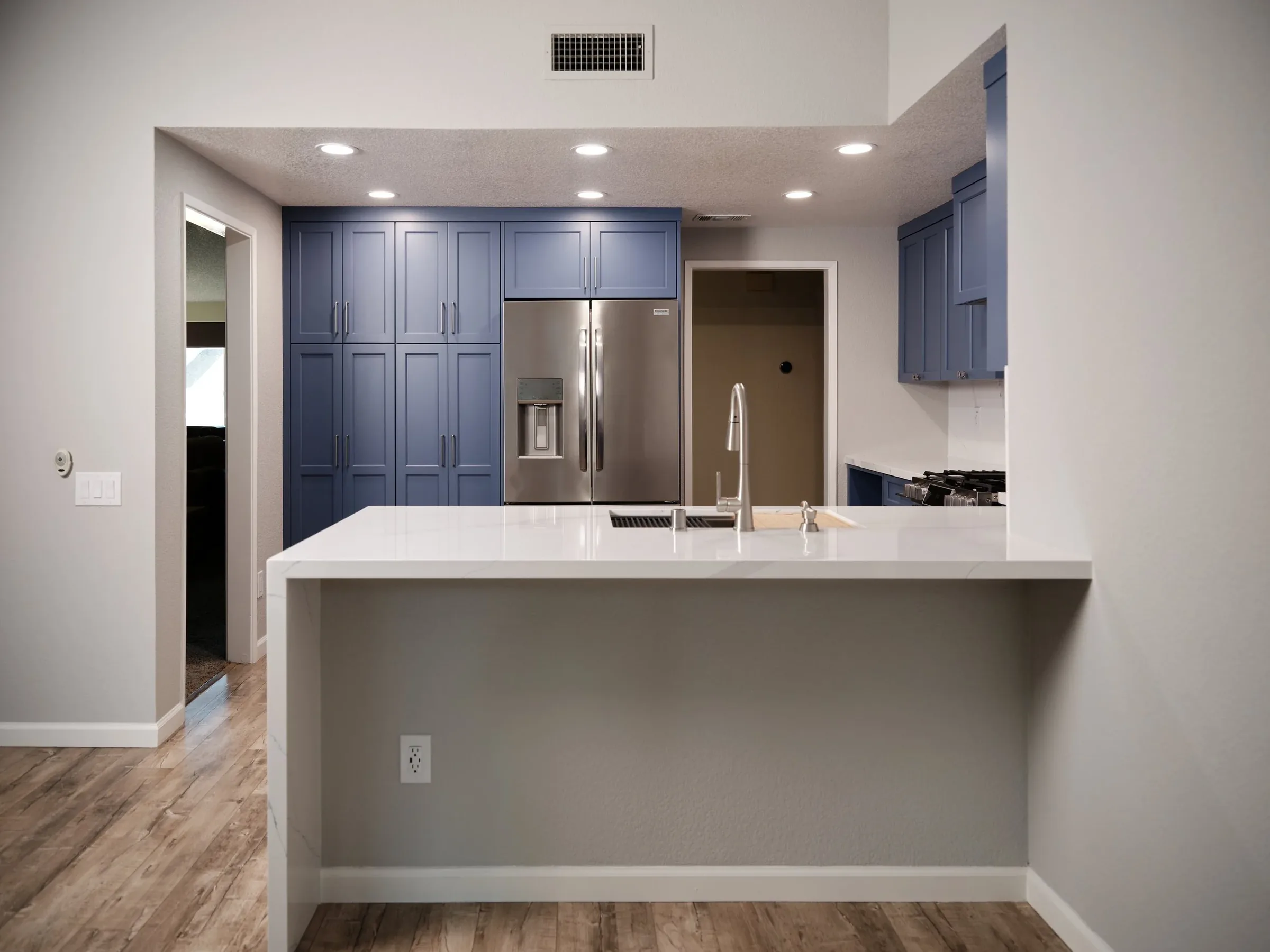 Modern kitchen with blue cabinets, stainless steel refrigerator, white island with sink, and hardwood flooring.