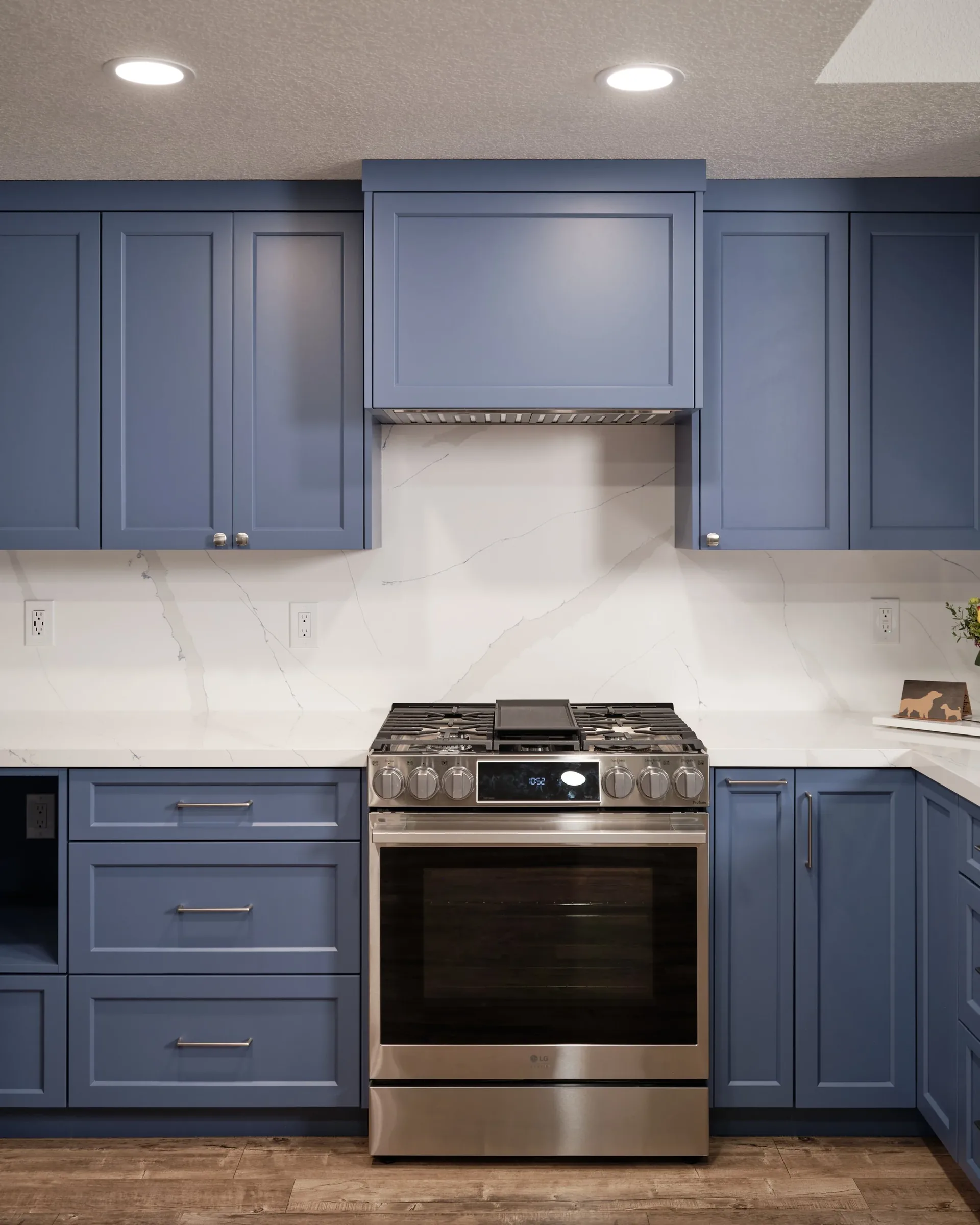 A modern kitchen featuring blue cabinets, a stainless steel LG oven, a marble backsplash, and recessed ceiling lighting.