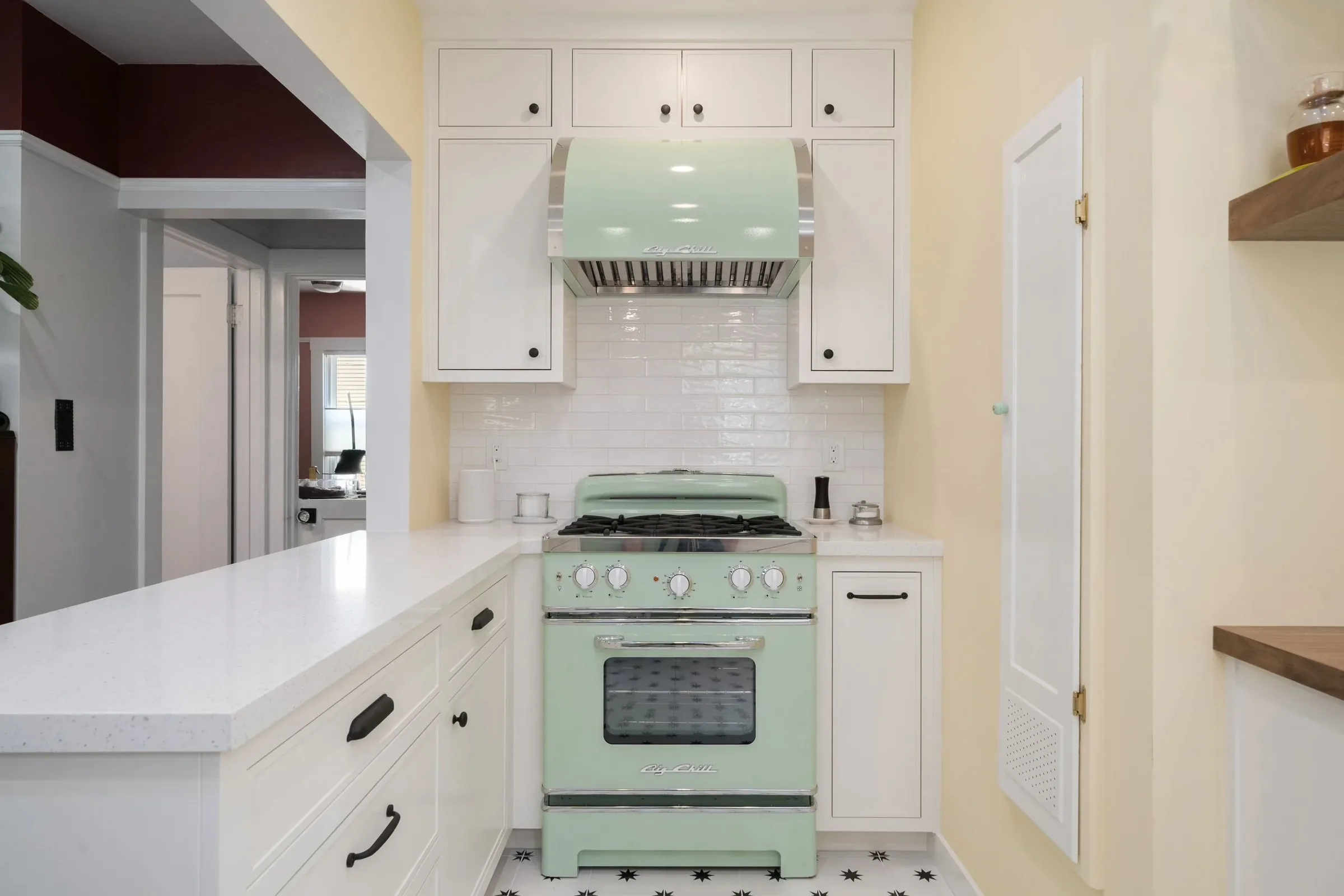 Mint green vintage stove with four burners in a kitchen with white cabinetry and a white subway tile backsplash.
