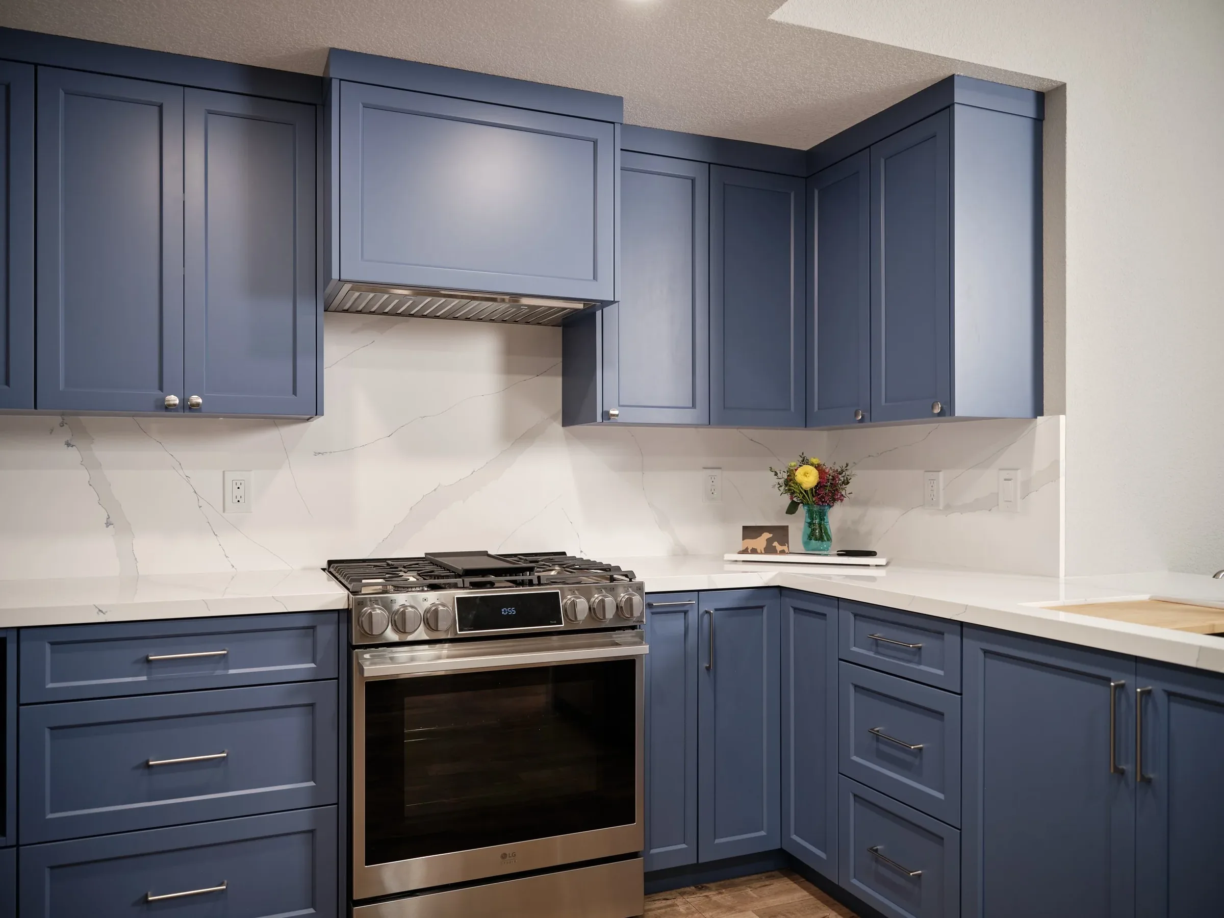 Kitchen with blue cabinets, stainless steel stove, marble backsplash, and a vase of flowers on the countertop.